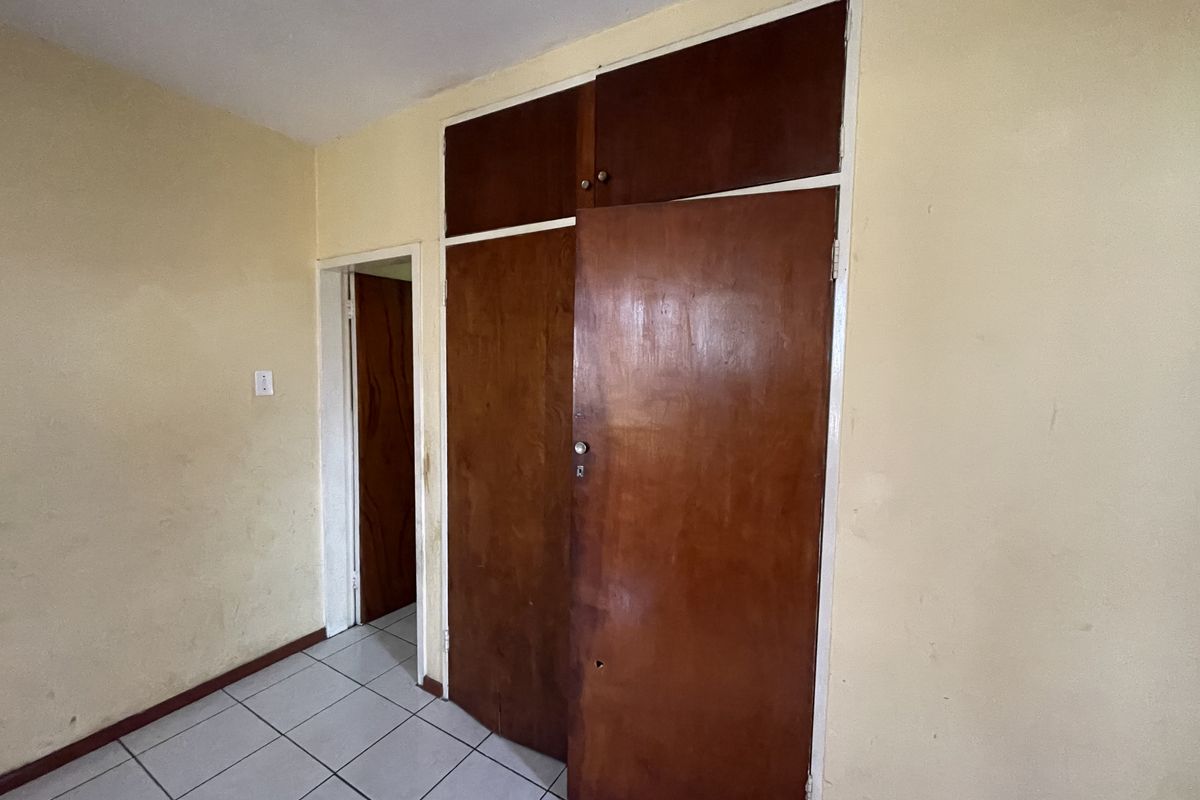 A vacant bedroom featuring tiled flooring and built-in wooden cupboards, requiring cosmetic updates to the walls and cabinetry.
