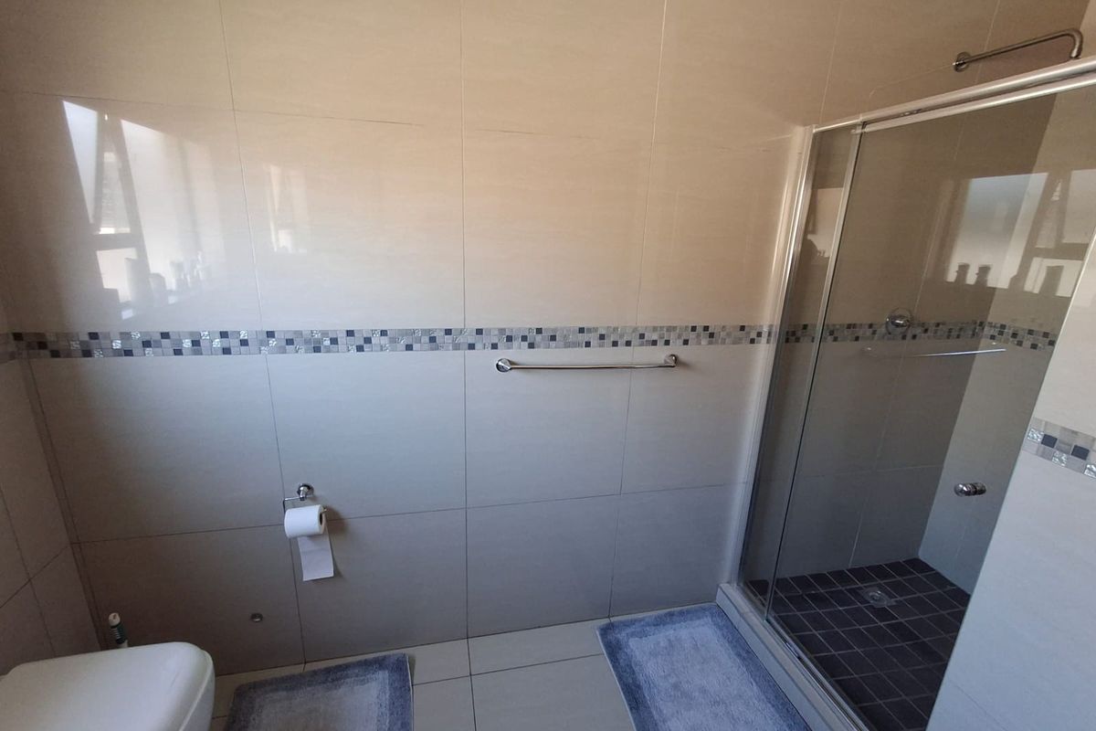 A clean, modern bathroom featuring a glass-enclosed shower, neutral wall and floor tiling, and a wall-mounted toilet.