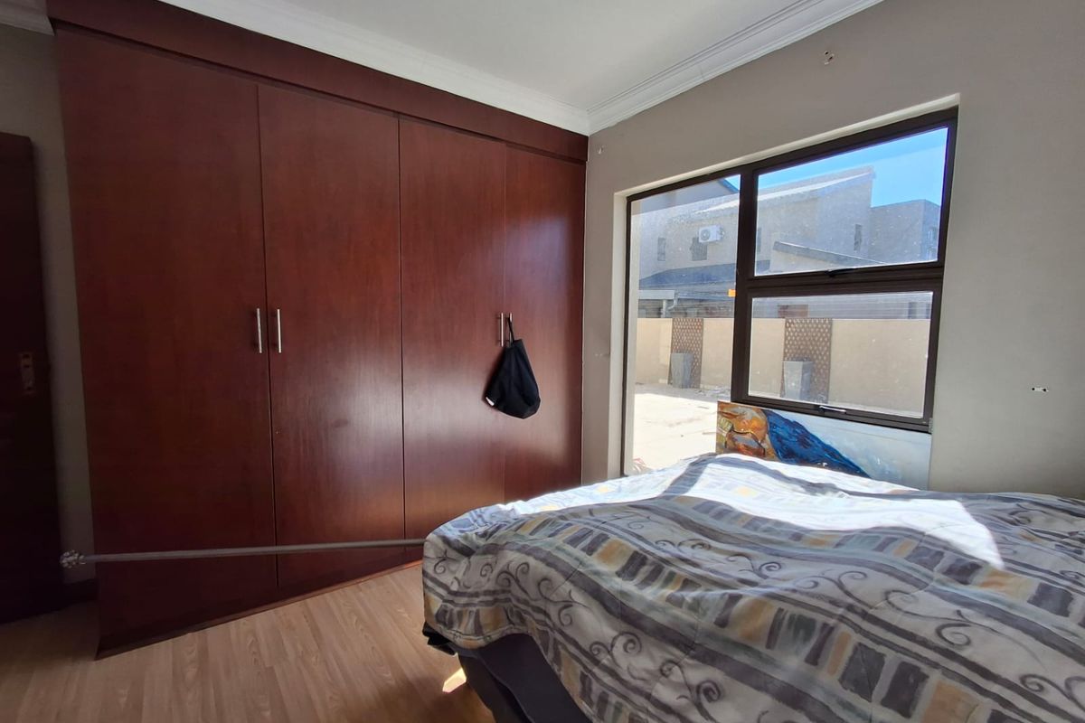 A bedroom featuring dark wood built-in cupboards, laminate flooring, and a large window providing natural light.