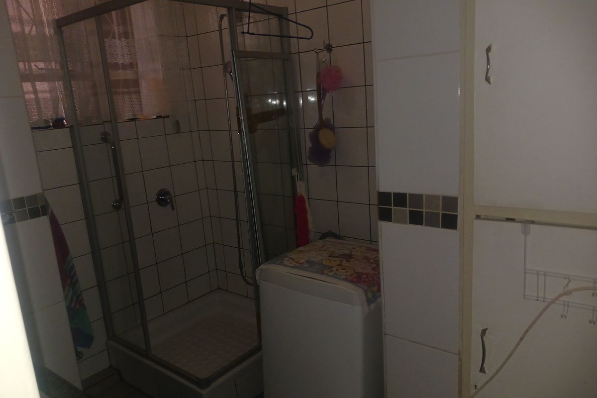 A functional bathroom featuring a corner shower enclosure with tiled walls and built-in storage cabinetry.