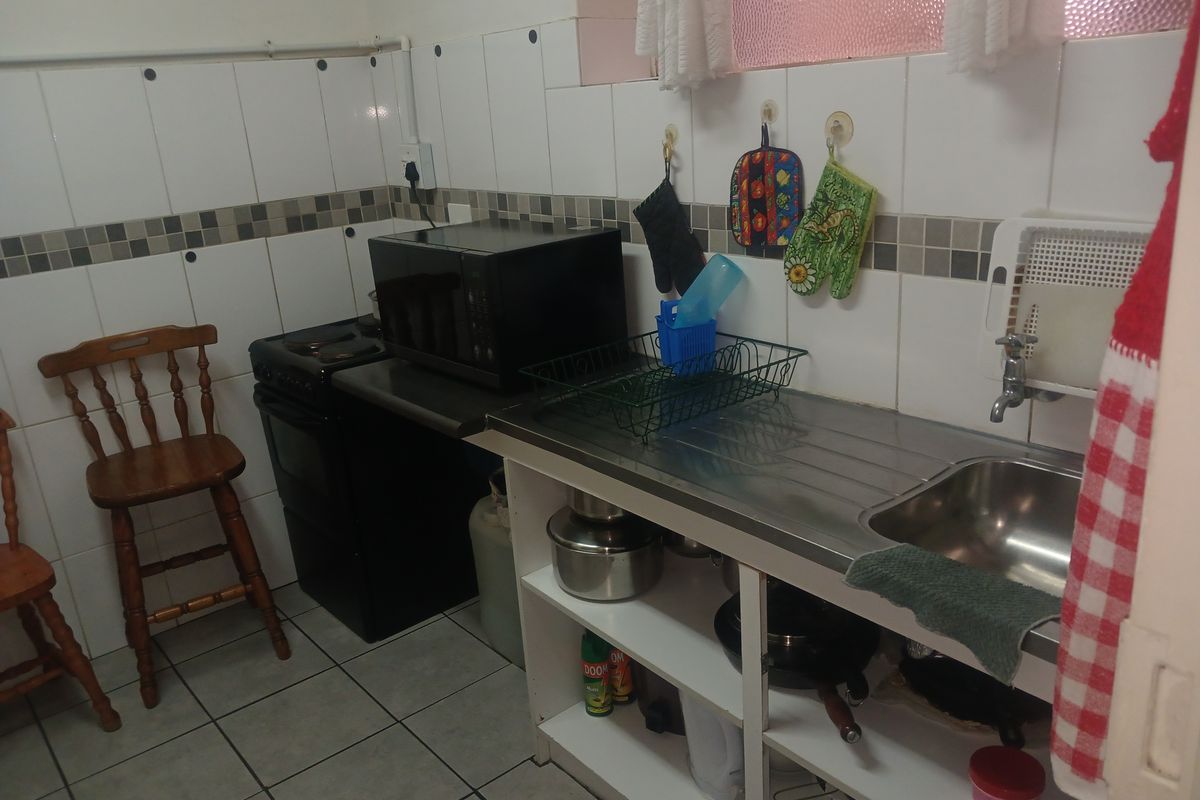 A compact kitchen featuring a stainless steel sink, tiled splashbacks, and a freestanding stove, offering a functional layout for basic culinary needs.