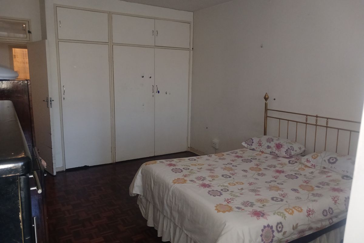 A bedroom featuring parquet flooring and built-in storage cupboards with overhead cabinetry.