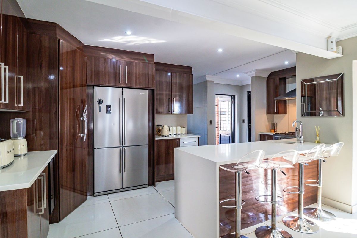 Modern kitchen featuring high-gloss dark wood cabinetry, white stone countertops, a central island with breakfast bar seating, and integrated stainless steel appliances.