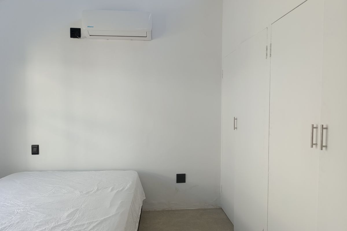 A clean bedroom featuring built-in cupboards, tiled flooring, and a wall-mounted split-system air conditioner.