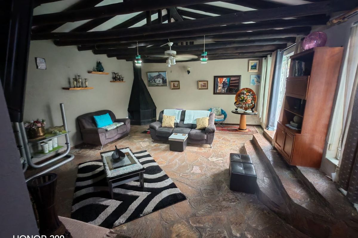 Spacious living room featuring rustic exposed timber ceiling beams, natural flagstone flooring, and a characterful corner fireplace.