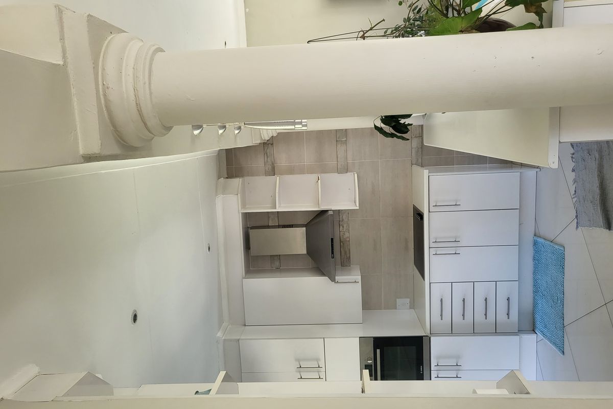 A clean, modern kitchen area featuring white built-in cabinetry, a tiled backsplash, and integrated appliances, viewed past a structural column.