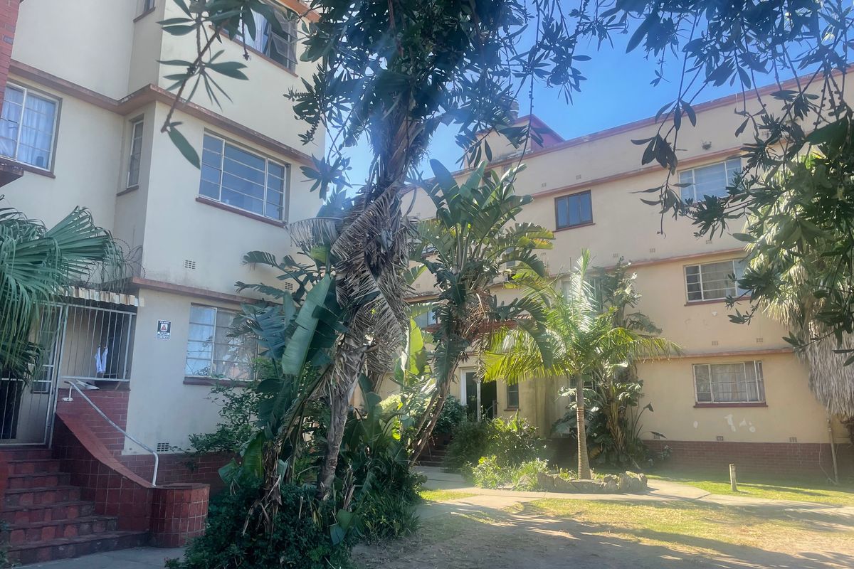 Exterior view of a multi-story apartment building featuring a shared garden area, brick staircases, and established landscaping.