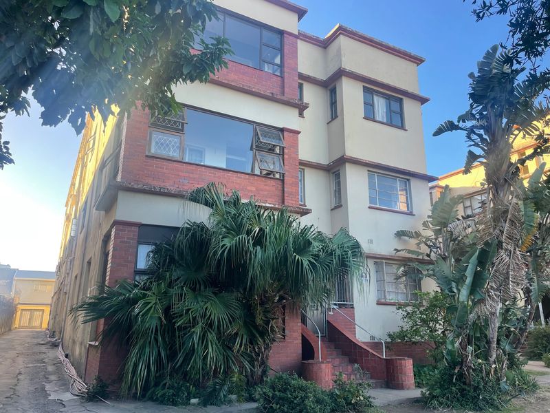 Front elevation of a multi-story apartment building featuring brick and plaster finishes with large casement windows and a concrete entrance staircase.