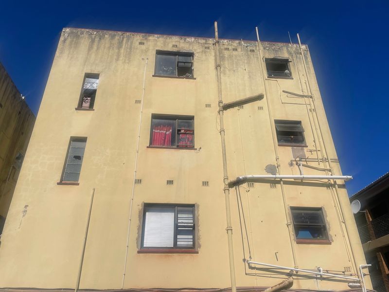 Rear elevation of a multi-story flat building showing significant exterior wall weathering, staining, and damaged window fixtures requiring maintenance.