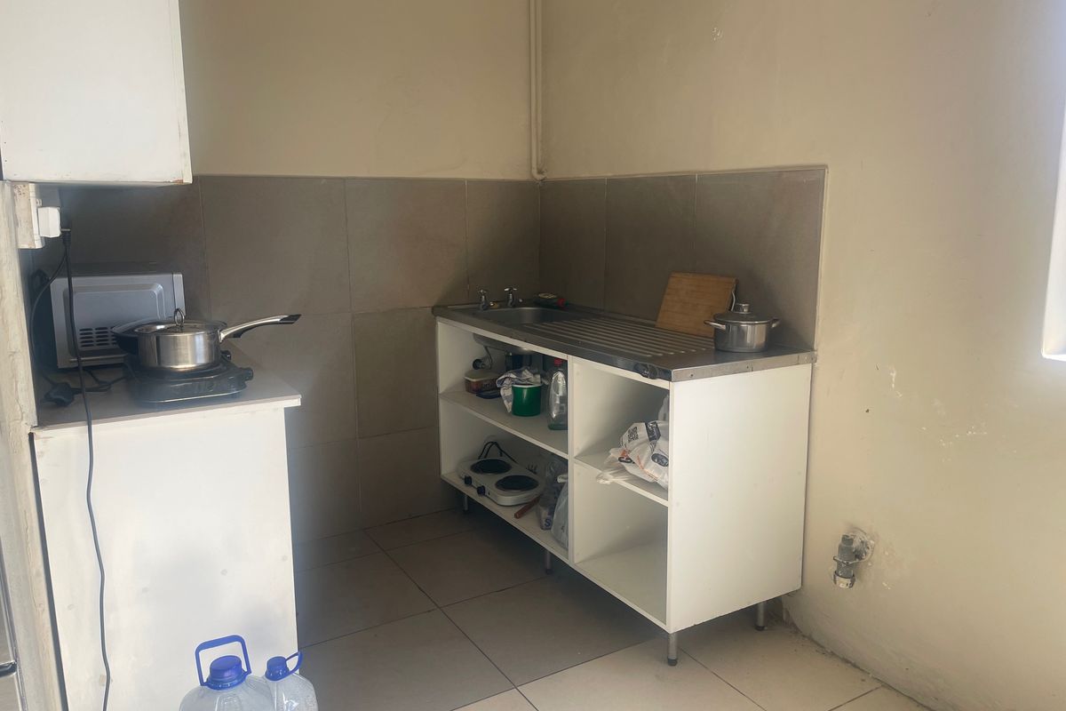 A compact kitchen area featuring a stainless steel sink, tiled splashback, and open shelving cabinetry with tiled flooring.