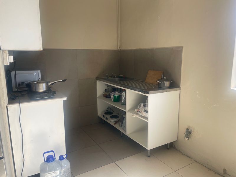 A compact kitchen area featuring a stainless steel sink, tiled splashback, and open shelving cabinetry with tiled flooring.
