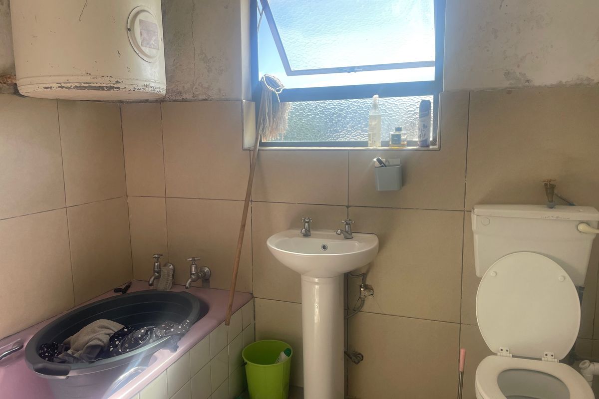A dated bathroom featuring a pedestal basin, toilet, and tiled walls, requiring renovation to address wall surface deterioration and modernize the fixtures.