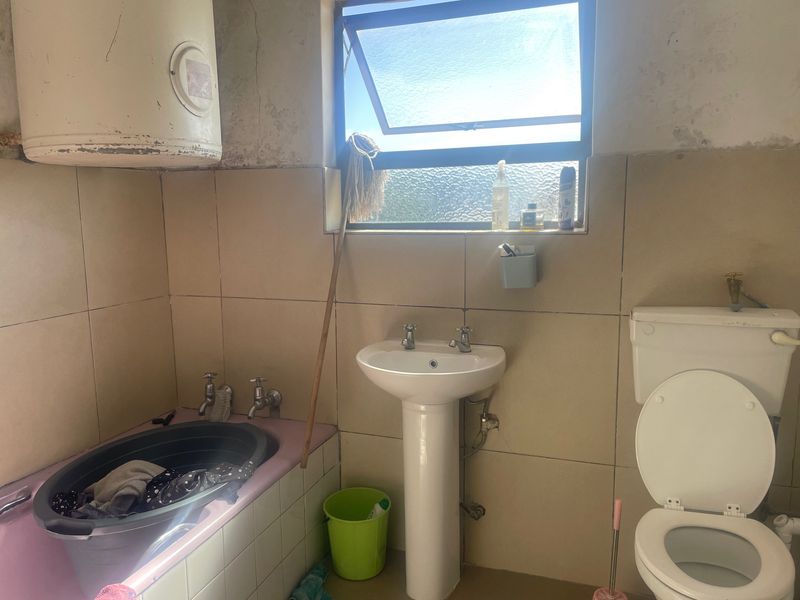 A dated bathroom featuring a pedestal basin, toilet, and tiled walls, requiring renovation to address wall surface deterioration and modernize the fixtures.