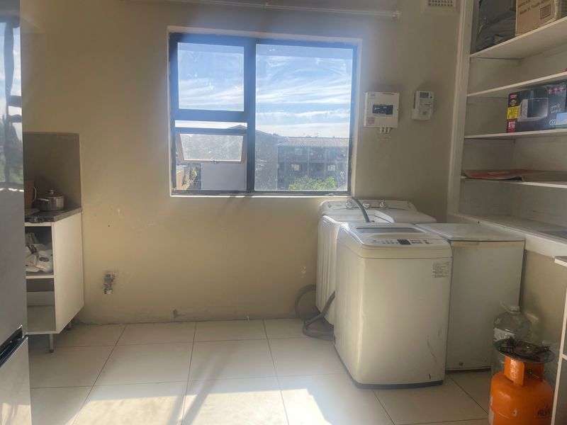 A functional laundry area featuring tiled flooring, built-in shelving, and dedicated plumbing connections for appliances.