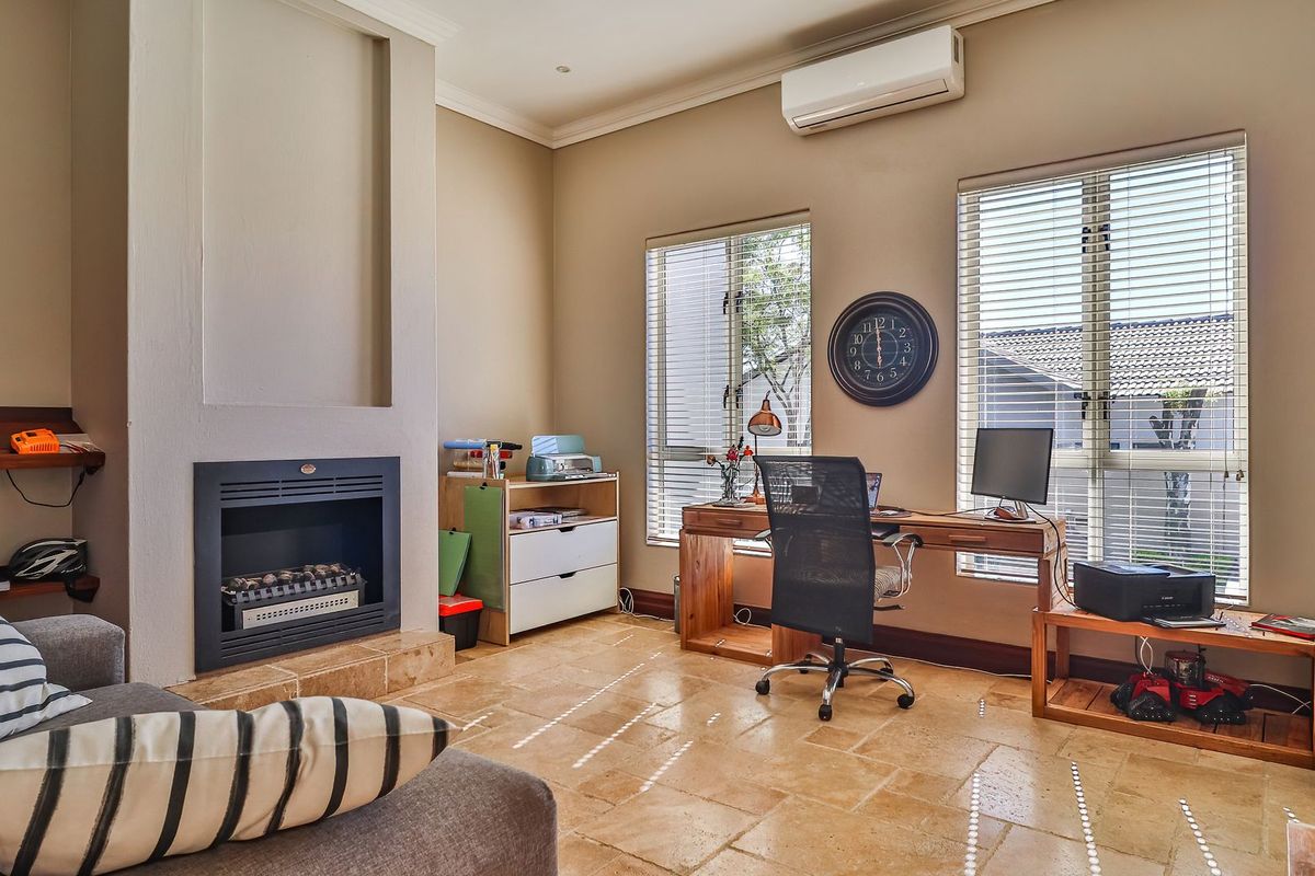 A well-maintained living room featuring stone tile flooring, a built-in fireplace, and a wall-mounted air conditioning unit, currently utilized as a home office space.