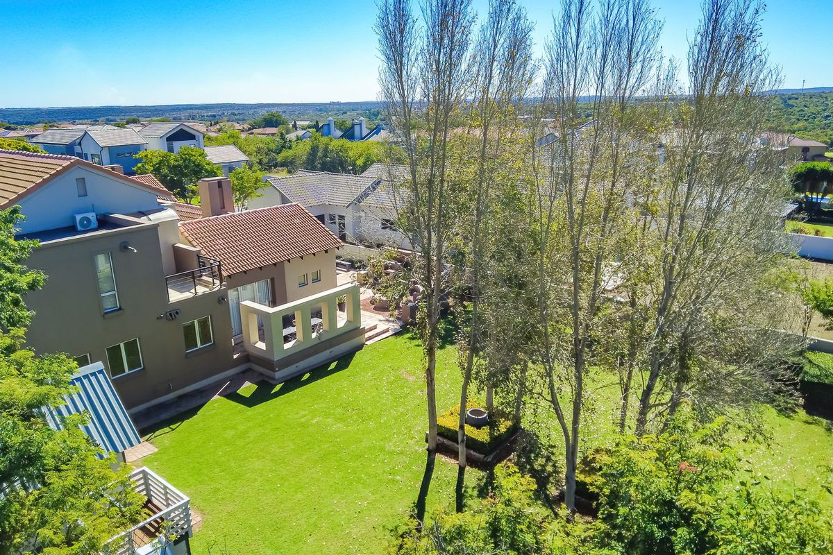 Aerial view of the property showcasing the rear elevation, tiled roof, balcony, and expansive landscaped garden area within a residential estate.