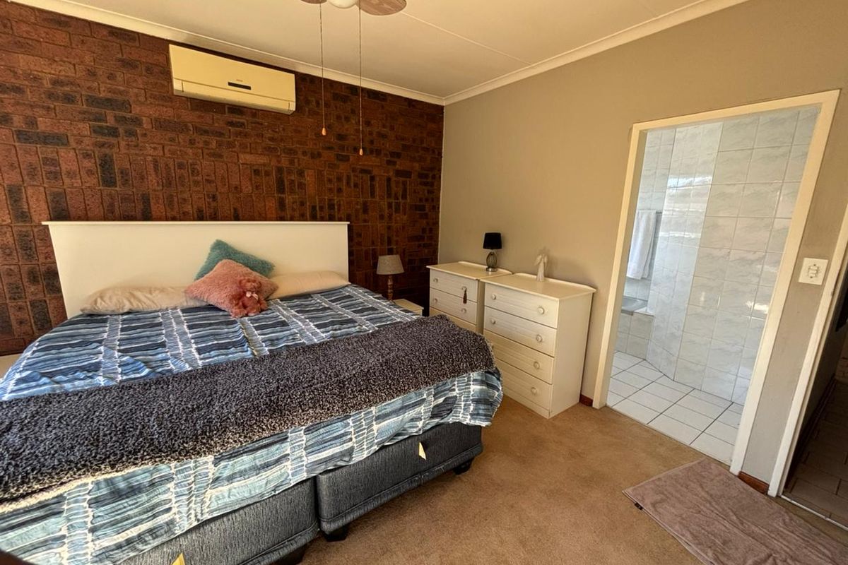 Spacious bedroom featuring a rustic face-brick accent wall, ceiling fan, wall-mounted air conditioner, and an en-suite bathroom with tiled finishes.