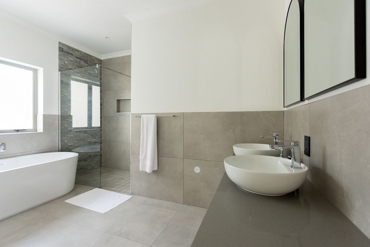 Modern bathroom featuring a freestanding bathtub, walk-in shower with stone tiling, and a dual vessel sink vanity with contemporary finishes.