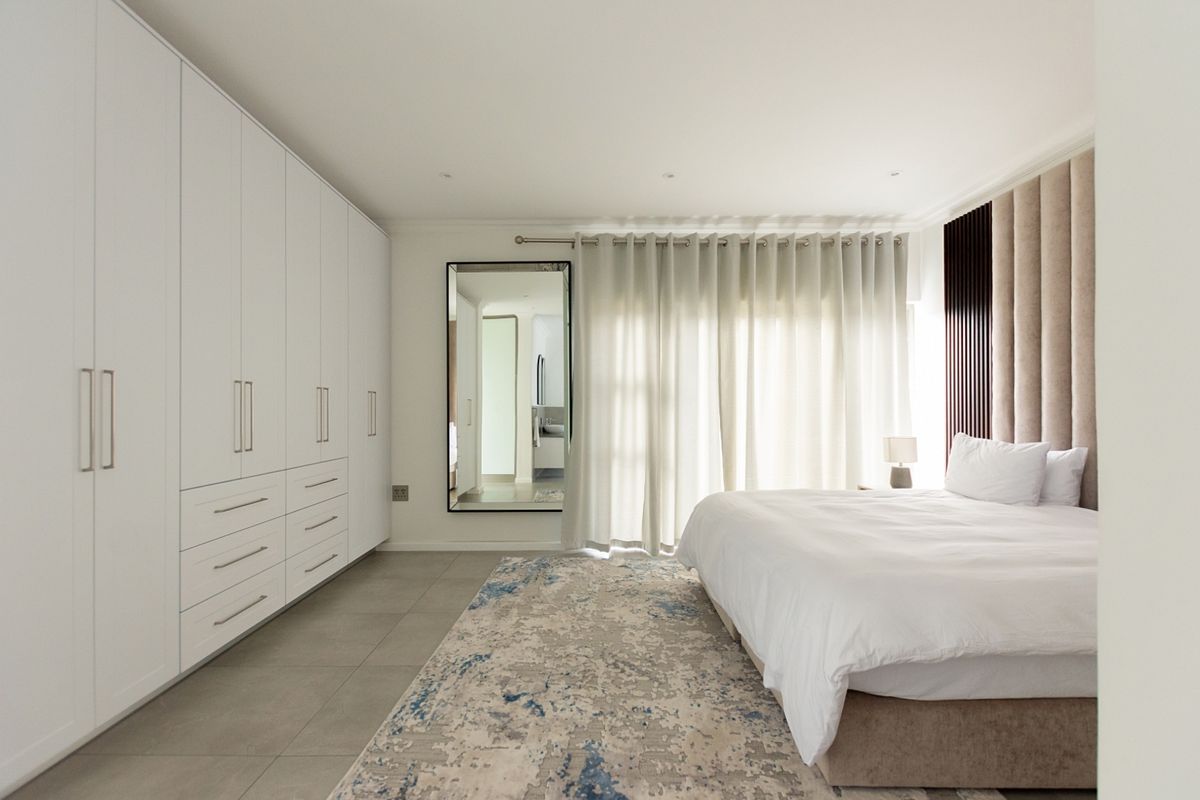 A modern, well-maintained bedroom featuring extensive built-in white cabinetry, tiled flooring, and a large upholstered headboard with integrated lighting.