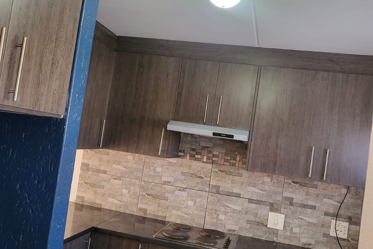 A functional kitchen featuring dark wood-look cabinetry, stone countertops, a tiled backsplash, and integrated appliances including an oven and hob.