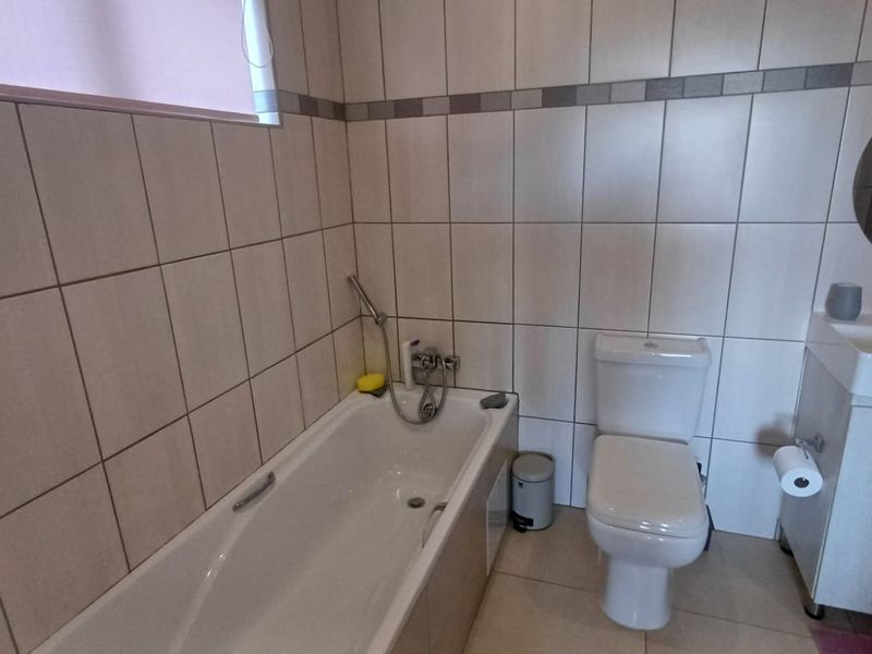 A functional bathroom featuring a bathtub with handheld shower, a toilet, and a vanity unit with a circular mirror and tiled walls.