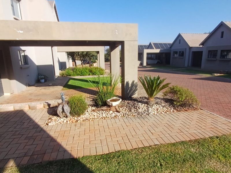 Front exterior view of a townhouse complex featuring a paved driveway, covered carport, and landscaped garden area.