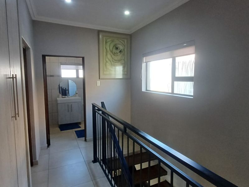 A bright upper-level hallway featuring tiled flooring, built-in storage cupboards, and a metal staircase railing, with direct access to an adjacent bathroom.