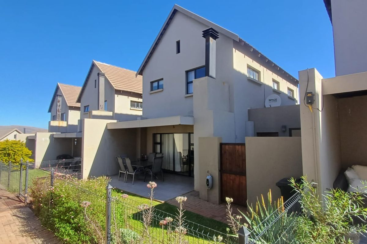 Rear view of the townhouse featuring a covered patio, paved outdoor area, and private garden space with perimeter fencing.