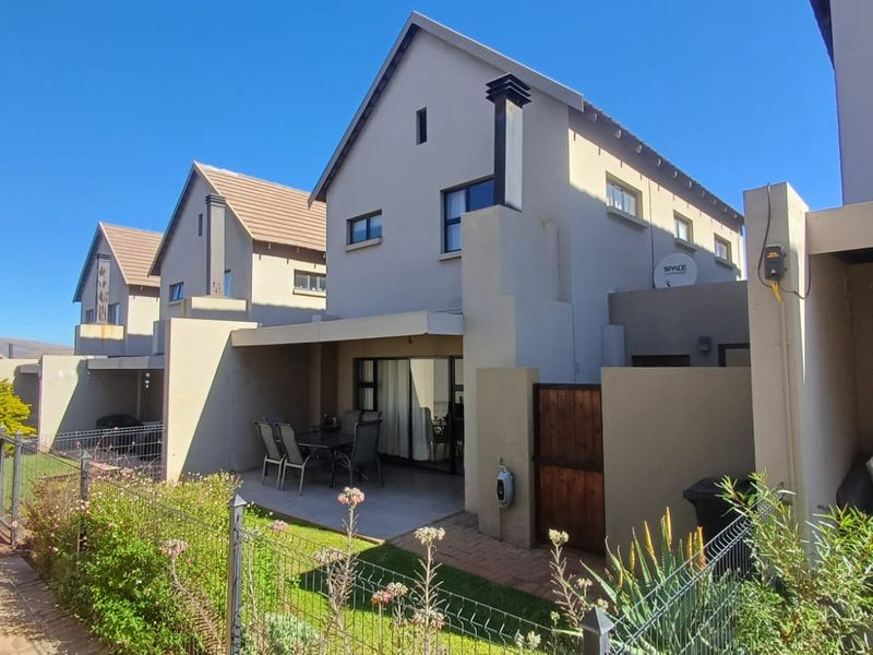 Rear view of the townhouse featuring a covered patio, paved outdoor area, and private garden space with perimeter fencing.