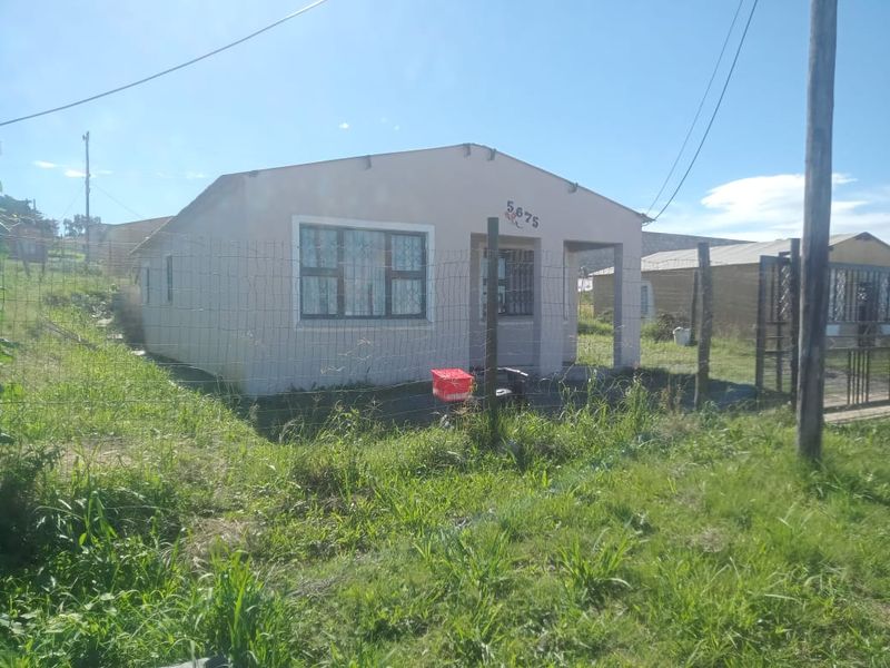 Front view of a single-story residential house featuring a concrete porch and wire mesh perimeter fencing on a grassed plot.
