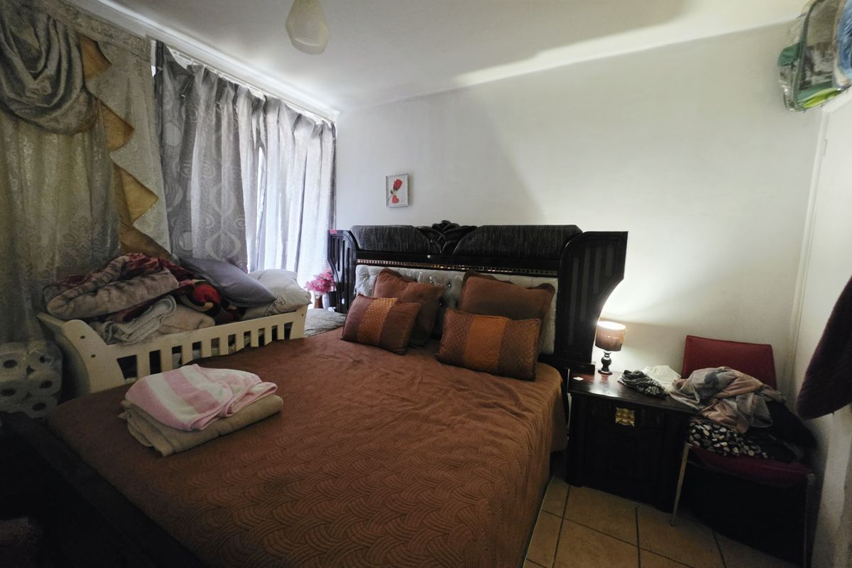 A bedroom featuring tiled flooring and window treatments, providing a functional space for rest.