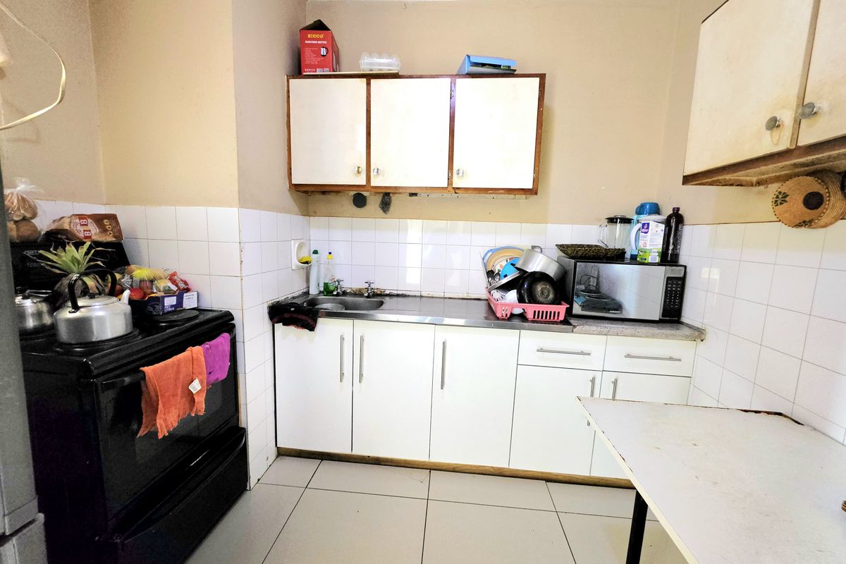 A functional kitchen featuring white cabinetry, a stainless steel sink, tiled backsplash, and tiled flooring, offering potential for modernization and cosmetic updates.