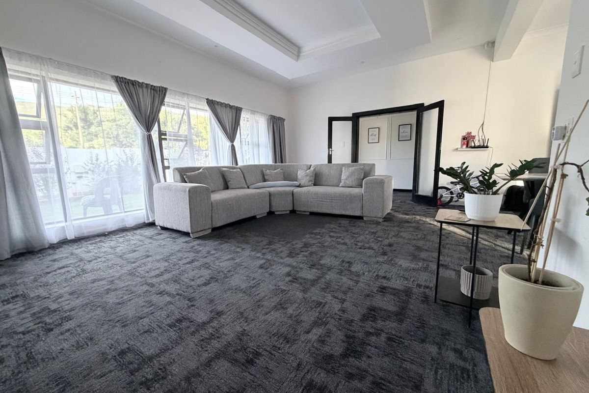Spacious living room featuring large windows with natural light, recessed ceiling detail, and dark carpeting.