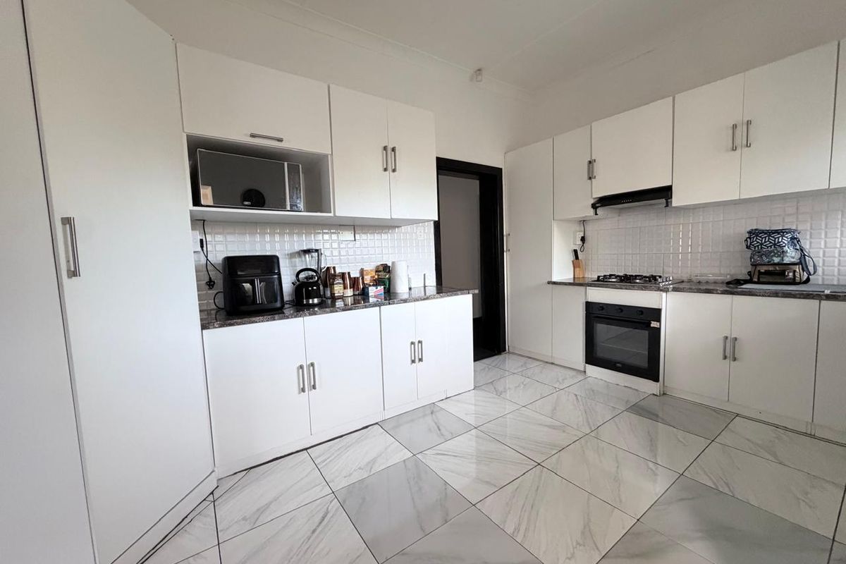 Modern kitchen featuring white cabinetry, marble-look tiled flooring, built-in oven, gas hob, and extractor fan with a clean, functional layout.