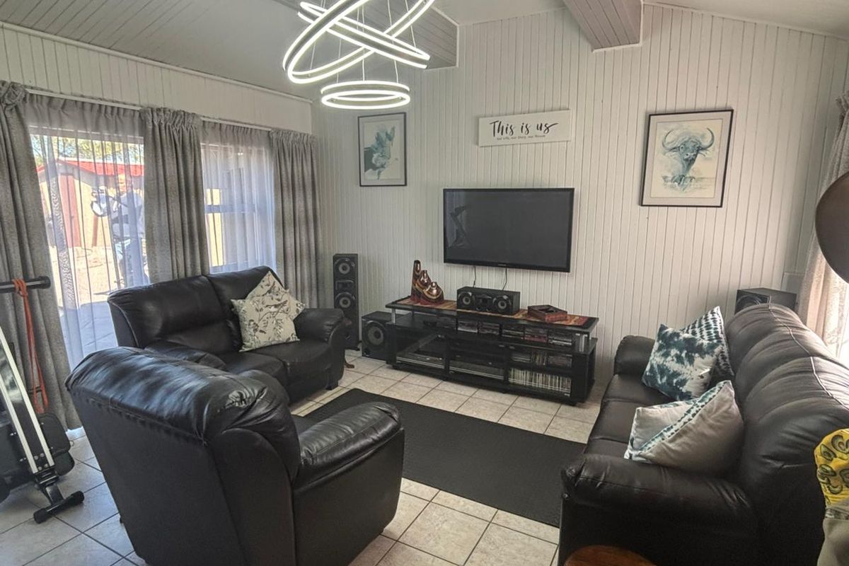 A comfortable living room featuring tiled flooring, timber-paneled walls, a vaulted ceiling, and sliding glass doors providing access to the outdoor area.