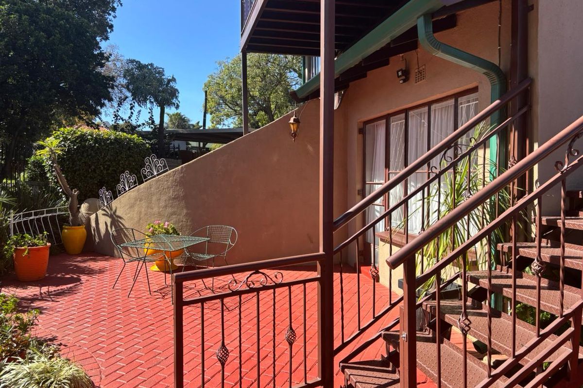 A paved rear patio area featuring a metal staircase leading to an upper level, surrounded by a low retaining wall and established garden elements.
