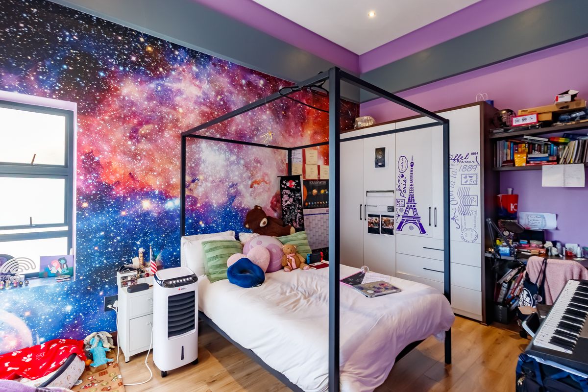 A bedroom featuring a galaxy-themed accent wall, built-in wardrobe storage, and laminate flooring, offering a personalized space with functional built-in cabinetry.