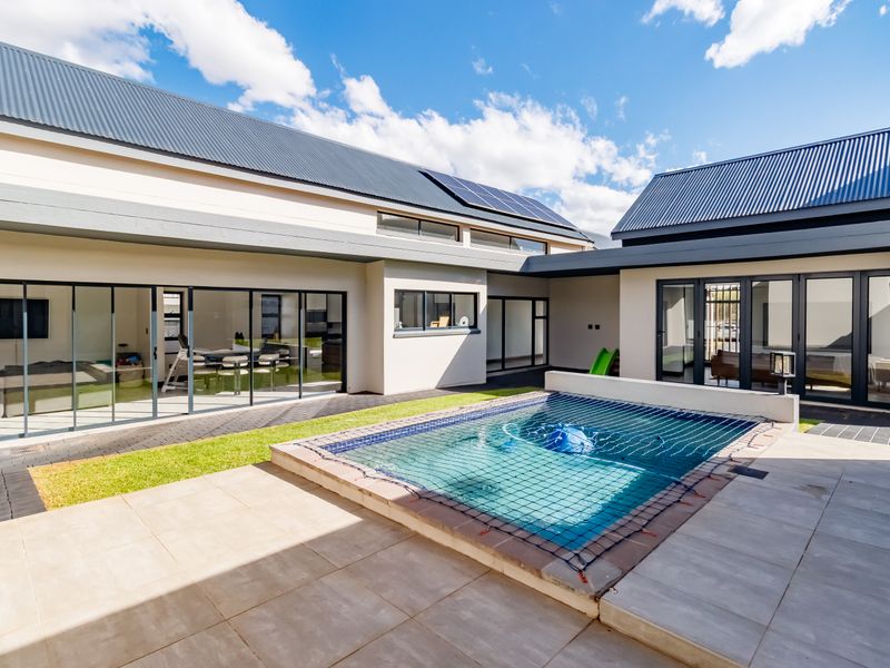 Modern courtyard featuring a swimming pool with safety net, surrounded by paved patio areas and large sliding glass doors leading into the home.
