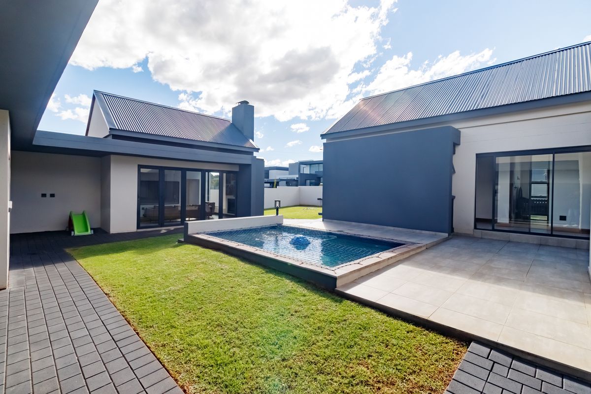 Modern rear exterior featuring a swimming pool, tiled patio area, manicured lawn, and contemporary architectural design with large sliding glass doors.