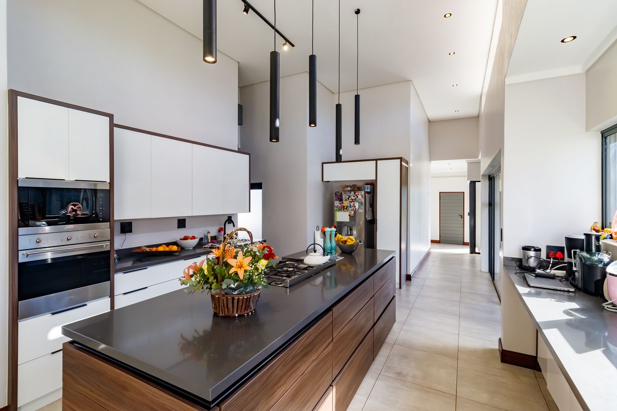 Modern kitchen featuring a large island with gas cooktop, stone countertops, sleek cabinetry, and contemporary pendant lighting in an open-plan layout.