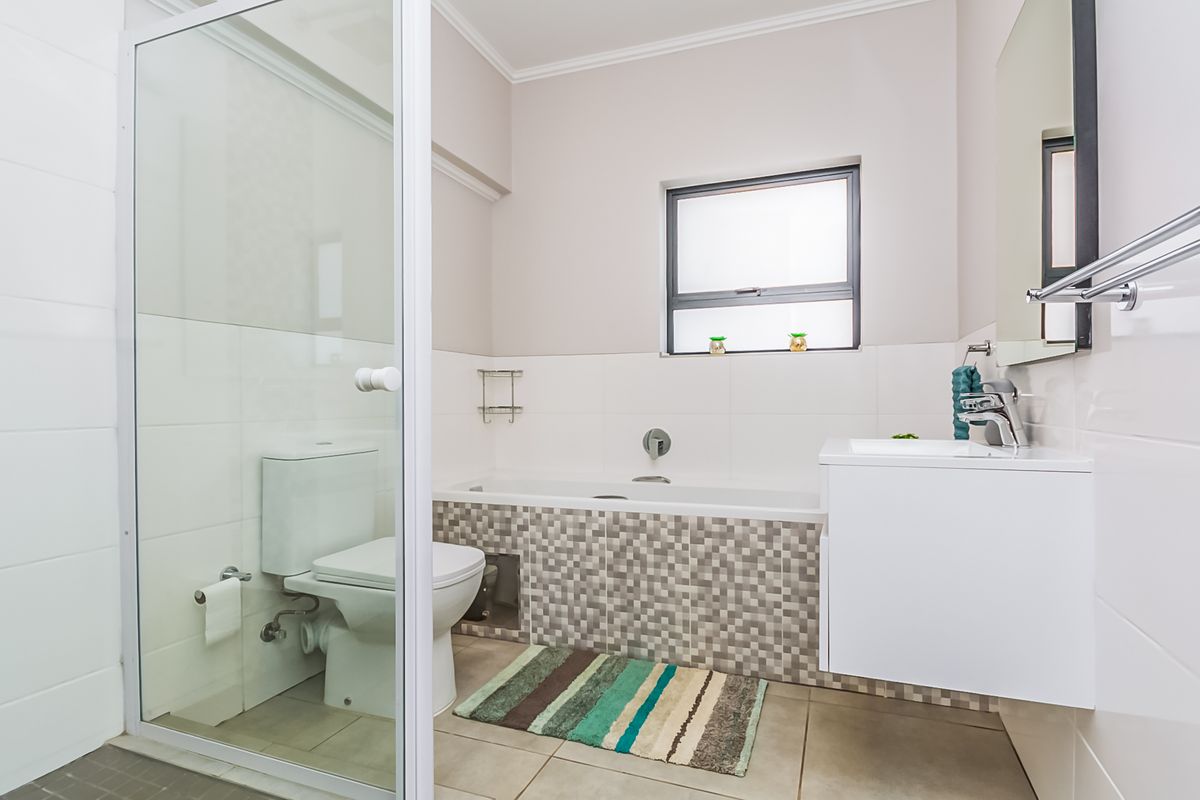 Modern bathroom featuring a glass-enclosed shower, a built-in bathtub with mosaic tile detailing, and a sleek wall-mounted vanity with a chrome mixer tap.