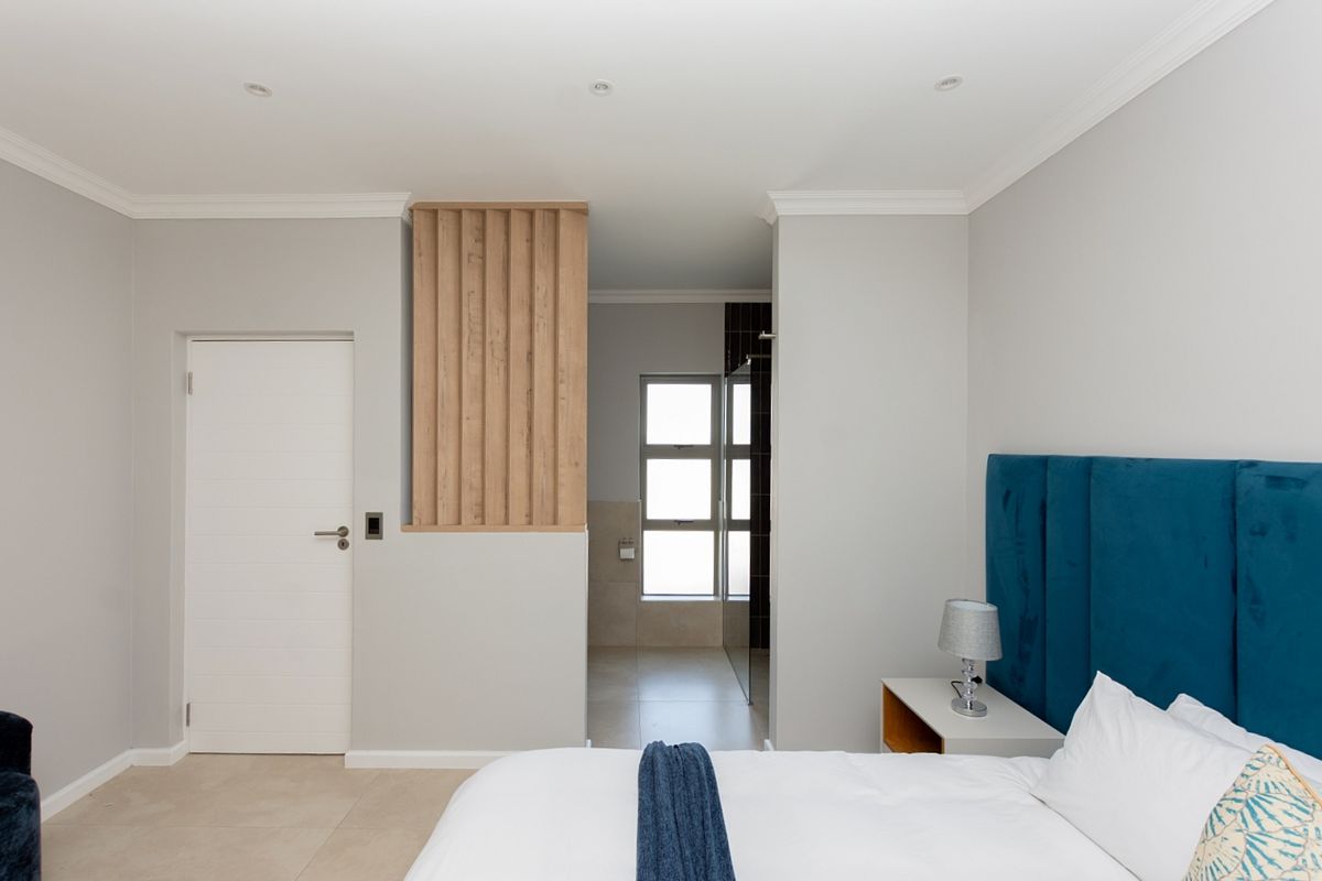 Modern bedroom featuring neutral tones, recessed lighting, decorative timber slat detailing, and direct access to an en-suite bathroom with tiled finishes.
