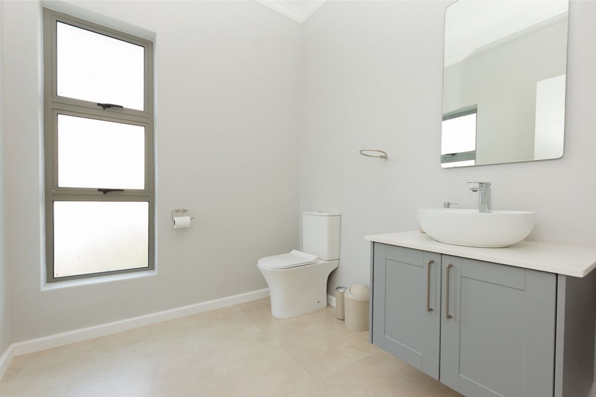 A clean, modern bathroom featuring a grey vanity cabinet with a vessel sink, a wall-mounted mirror, and a contemporary toilet.