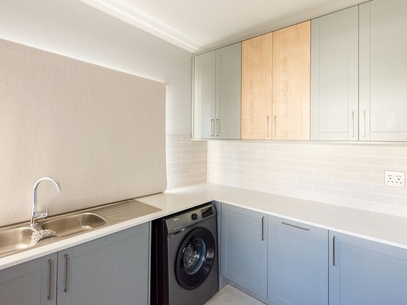 Modern laundry room featuring sleek two-tone cabinetry, stone countertops, subway tile backsplash, and a stainless steel sink with integrated washing machine.