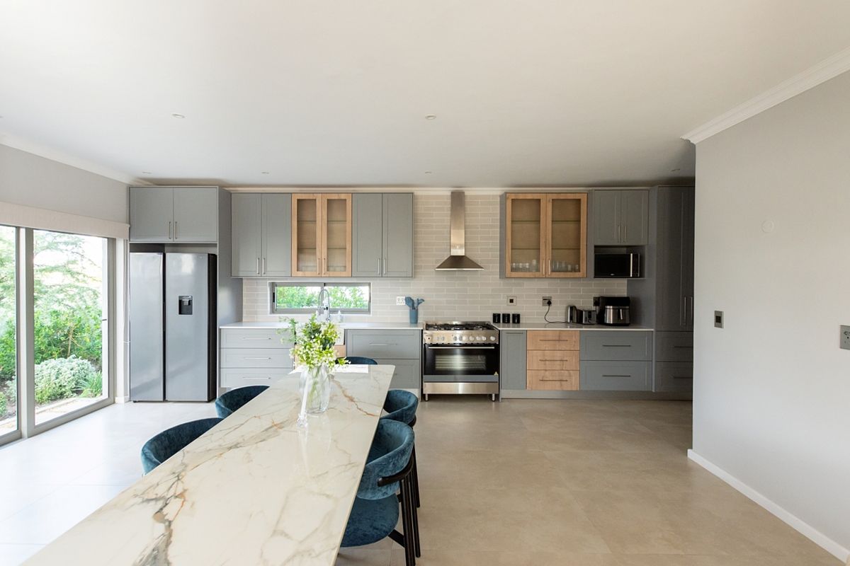 Modern kitchen featuring grey and wood-toned cabinetry, stone countertops, stainless steel appliances, and direct access to the garden through sliding glass doors.