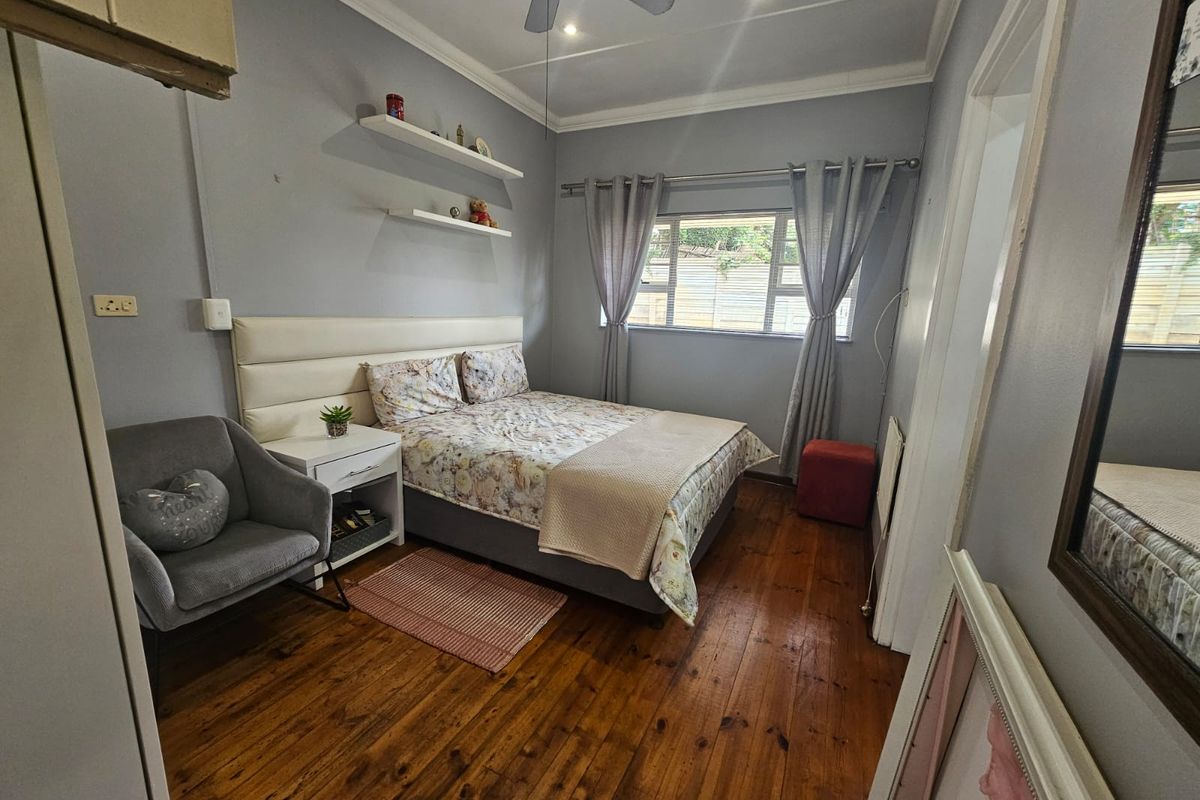 A cozy bedroom featuring polished timber flooring, a built-in upholstered headboard, floating shelves, and a ceiling fan.