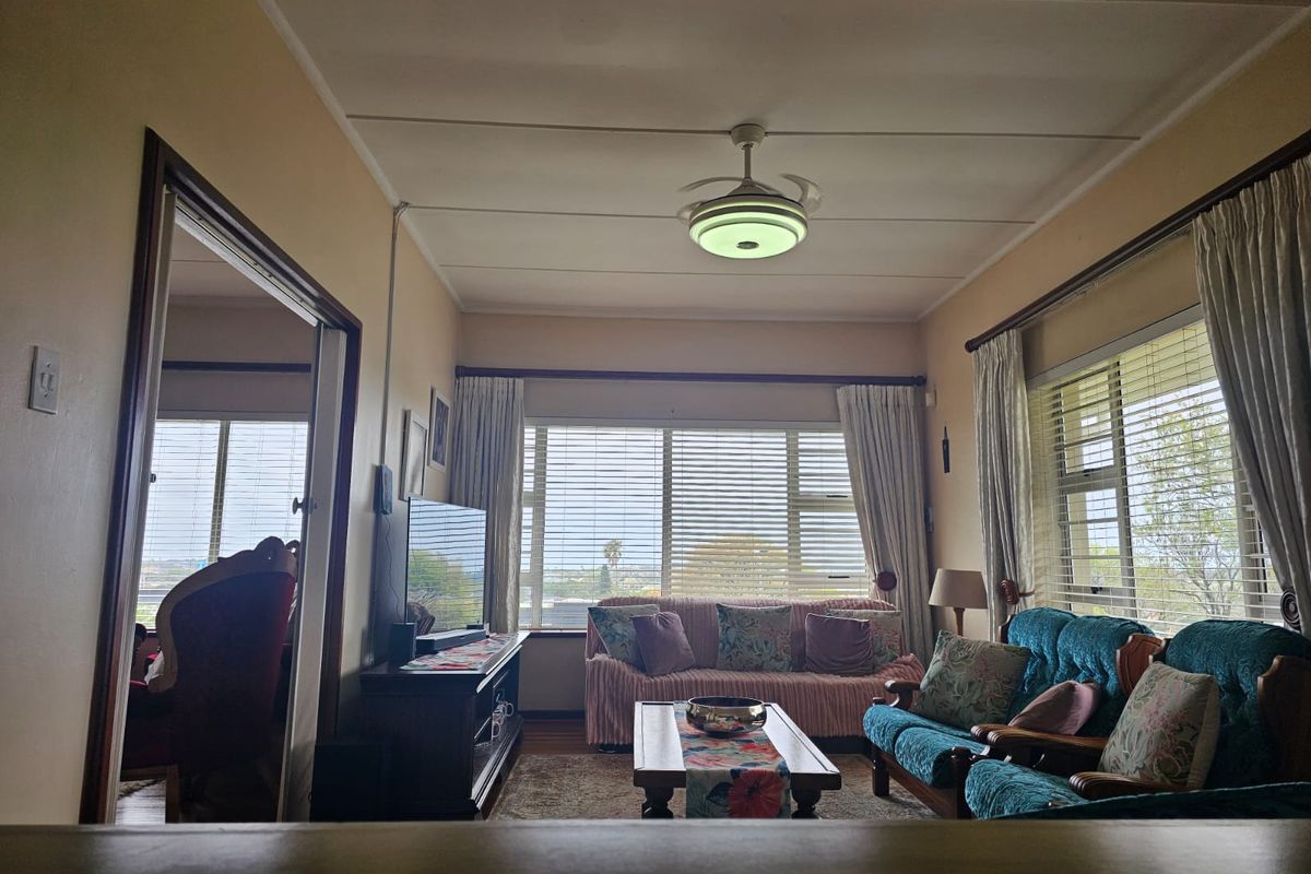 A comfortable living room featuring large windows with natural light, a ceiling fan, and hardwood flooring, offering a classic and functional living space.