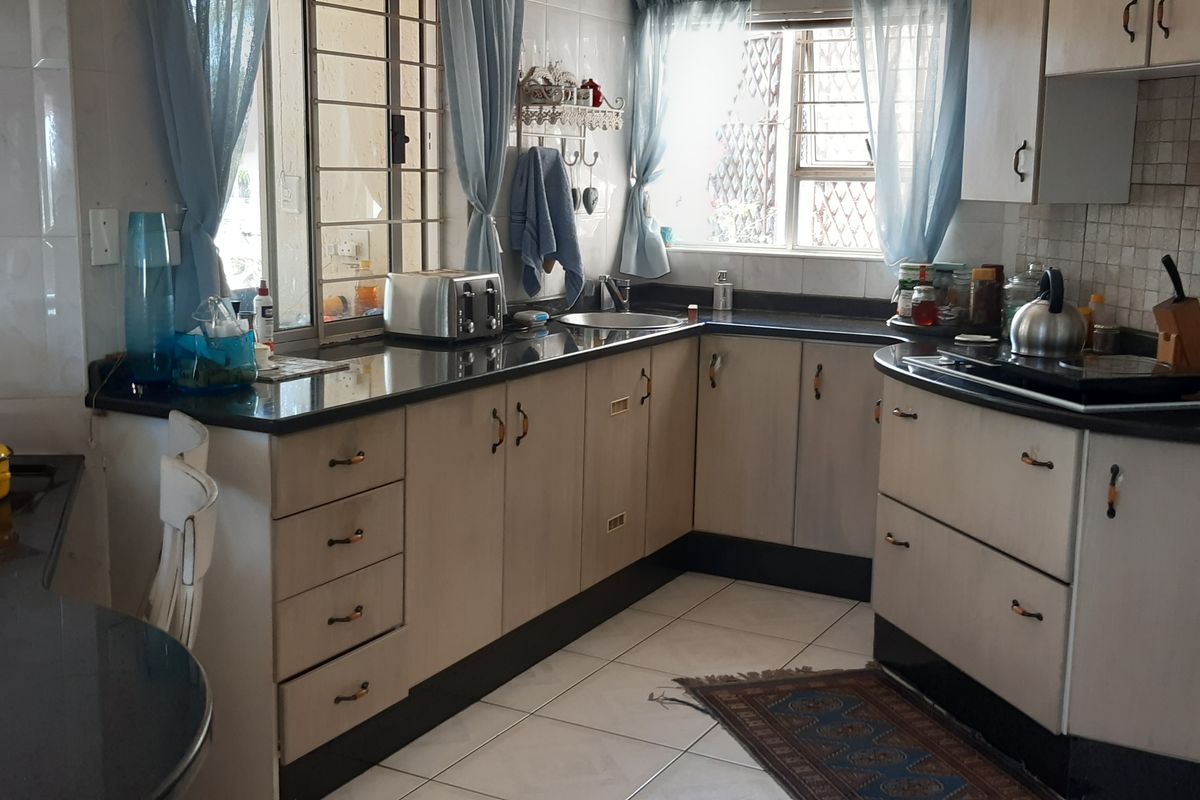Functional kitchen featuring light-toned cabinetry, dark granite countertops, integrated double wall oven, and ceramic hob with tiled flooring and security window bars.