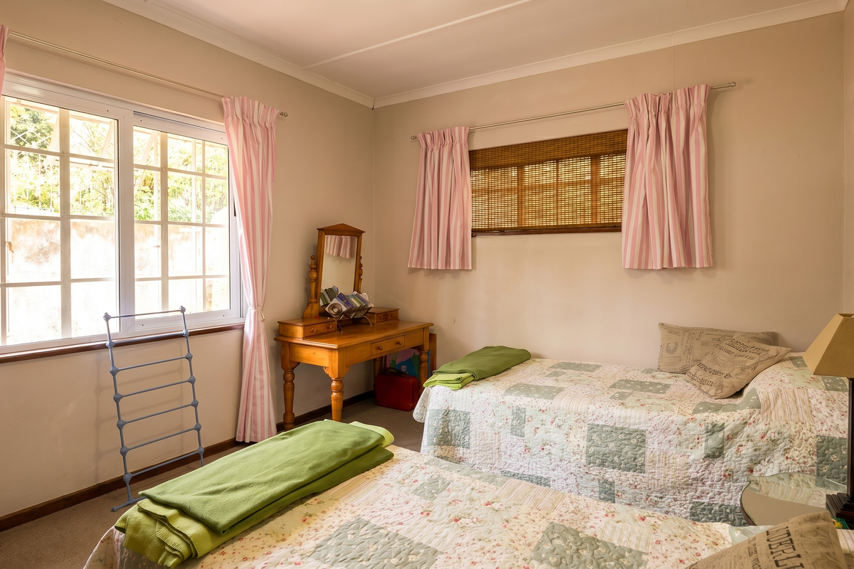 A well-lit bedroom featuring neutral walls, carpeted flooring, and dual windows with classic window treatments.