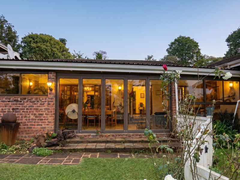 Rear view of the house featuring a brick facade, large folding glass doors opening onto a tiled patio, and an integrated water tank.